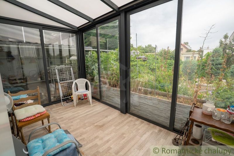 A cottage with a glass-enclosed terrace and a floor with a wooden decor, overlooking the garden.
