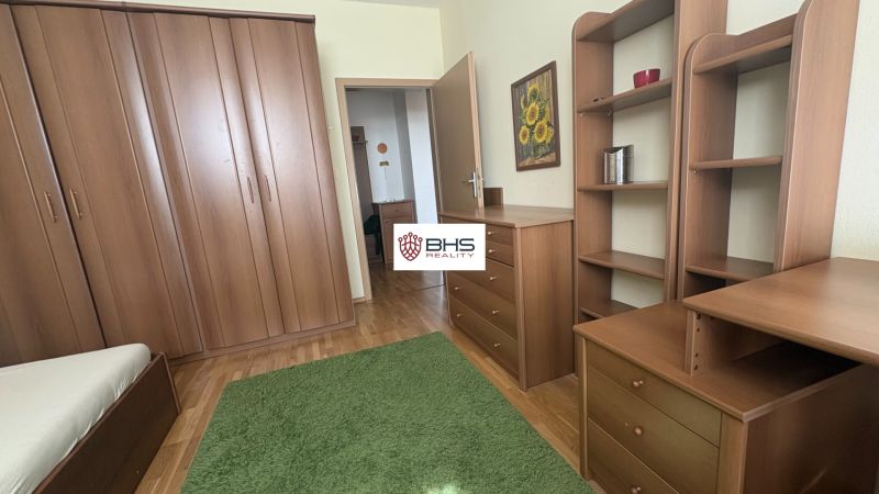 A bedroom in a two-room apartment with wooden furniture, a green carpet, and a floor with a wooden decor.