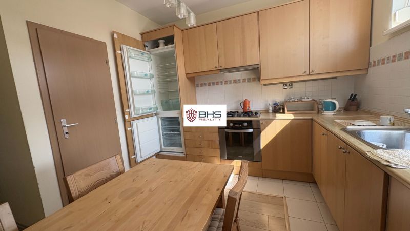 A kitchen in a 2-room apartment with built-in appliances, wooden cabinets, and a floor with a wooden decor.