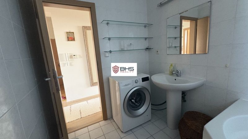 A bathroom in a 2-room apartment with a mirror, sink, and washing machine on the tiles.