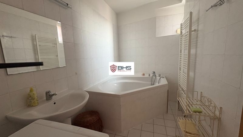 A bathroom with a corner bathtub and white tiles in a two-room apartment.