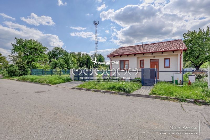 A family house on the street in Kátlovce with an antenna, grass, and a cloudy sky.