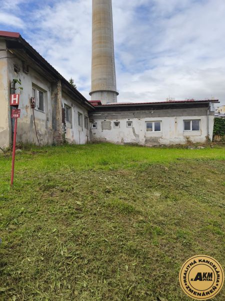 A building in Žiar nad Hronom with an industrial chimney, surrounded by a grassy area, suitable for warehouses and halls.