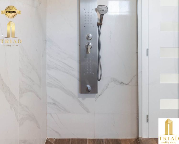 Shower enclosure with marble tiles and a wood-patterned floor in a family house.