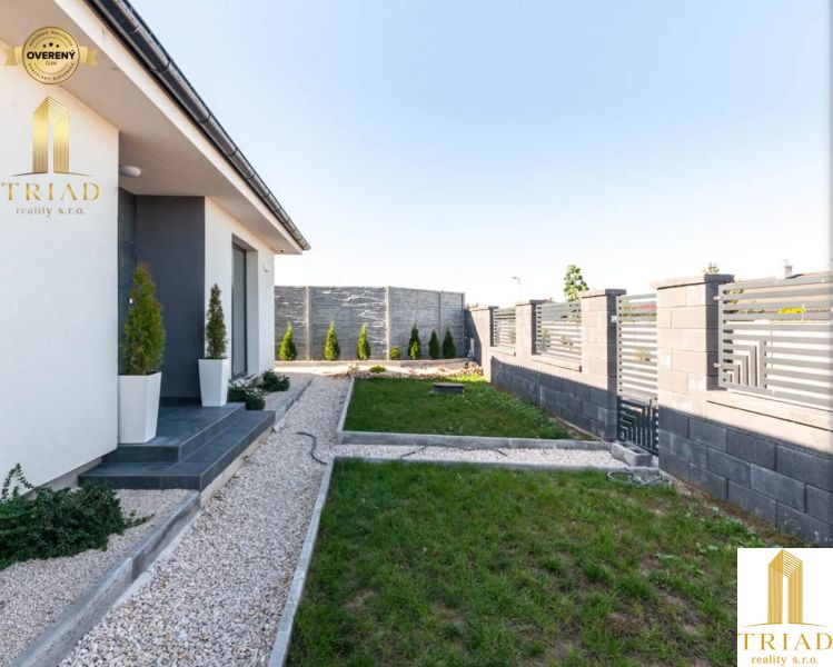 A family house in Bajč with a landscaped garden, a hedge, and a stone pathway.