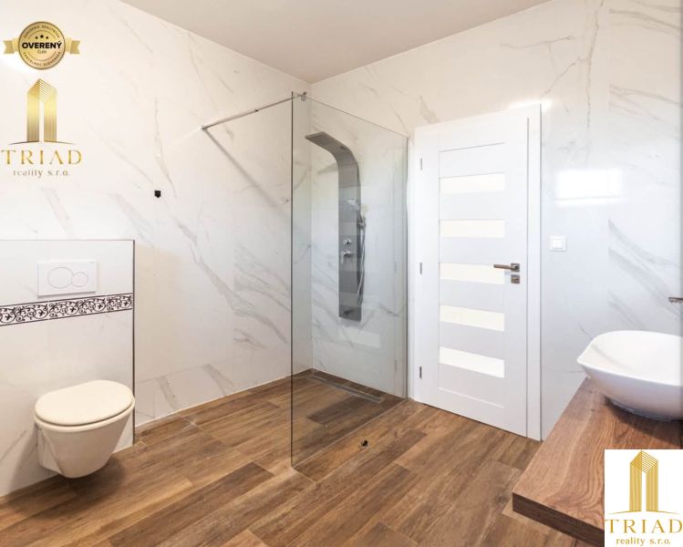 A bathroom with a glass shower enclosure, toilet, and wooden decor flooring in a family house.