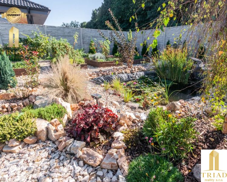 A garden with a pond in the exterior of a family house in Bajč, surrounded by greenery and stones.