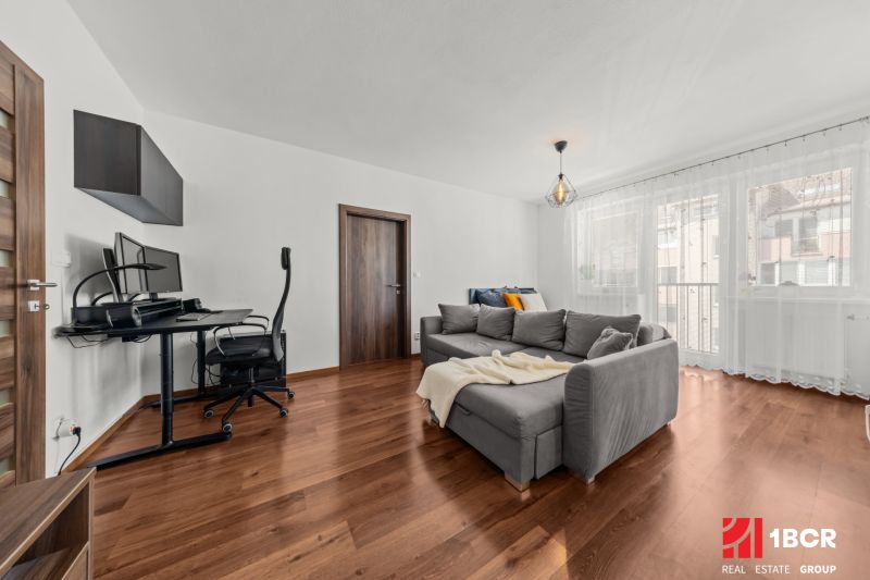 Living room with a sofa, desk, and wood-patterned floor in a two-room apartment.