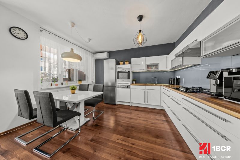 The kitchen of a two-room apartment with white furniture and a floor with a wood decor.