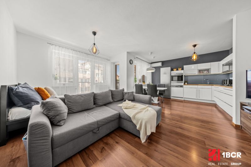 Living room and kitchen in a 2-room apartment with a wooden decor floor and light furniture.