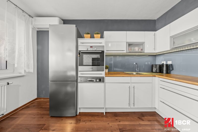 A kitchen with white cabinets and a wood-patterned floor in a two-room apartment.