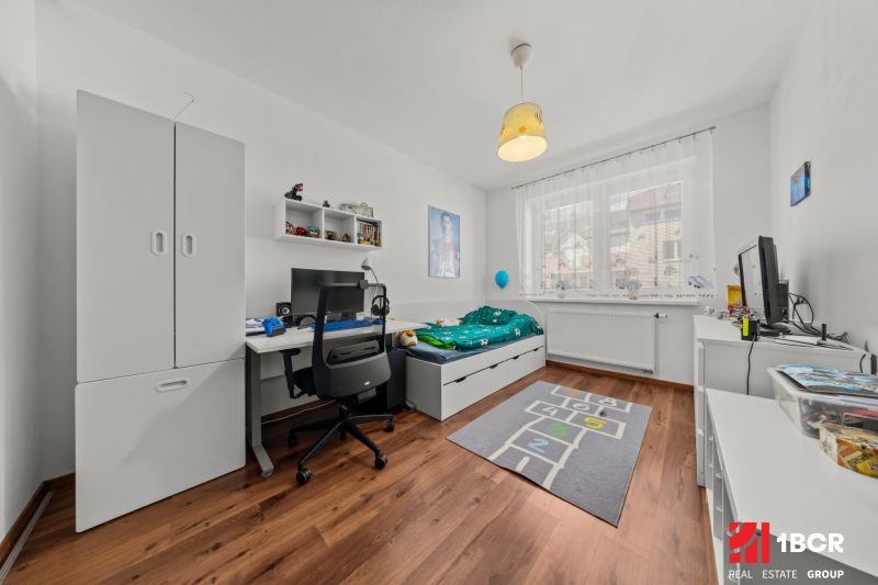 Children's room with a wooden decor floor in a 2-room apartment, a computer desk, and a bed.