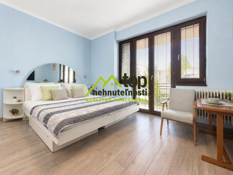 A bedroom in a family house with a wood-patterned floor and large windows.