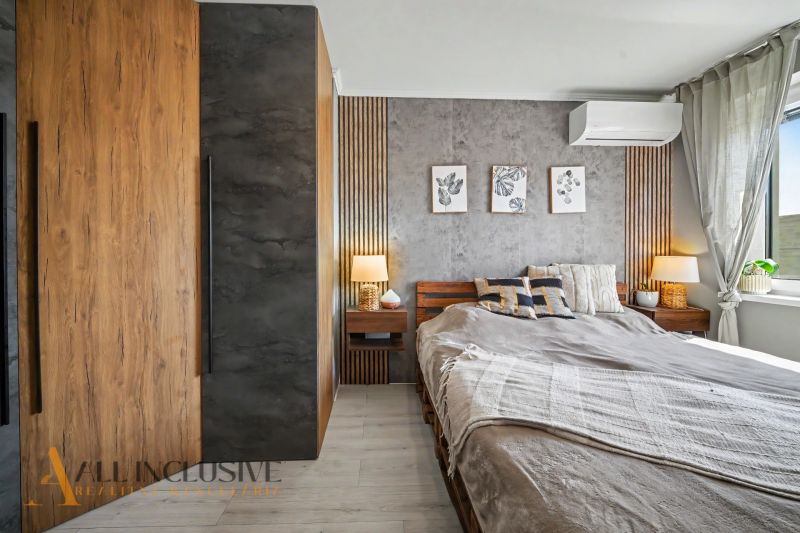 Bedroom in a three-room apartment with a wooden decor floor, a bed, and decorative paintings.