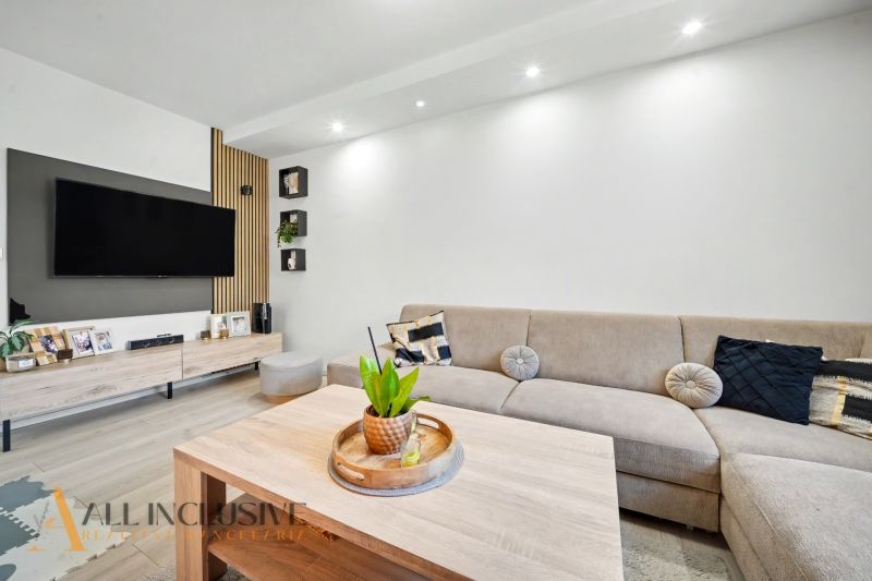 Living room in a three-room apartment with a corner sofa and a TV on the wall.