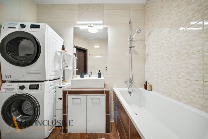 A bathroom with a bathtub, washing machine, dryer, and sink creates comfort in a 3-room apartment.