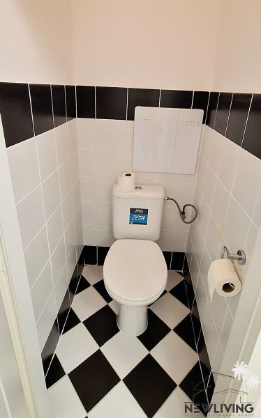 A toilet in a 2-room apartment with black and white tiles on the wall and floor.
