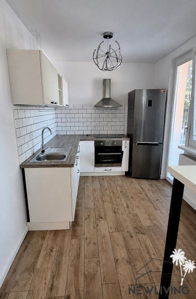A kitchen in a 2-room apartment with appliances and a wooden decor floor.