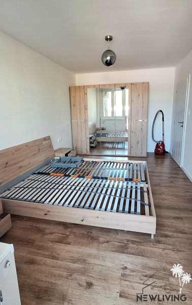 A bedroom in a two-room apartment with a wooden-decor floor, a bed, and a wardrobe.