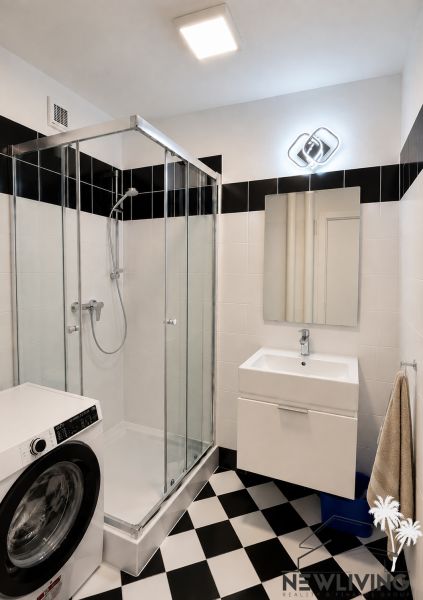 Bathroom in a 2-room apartment with a washing machine, shower corner, and black-and-white tiles.