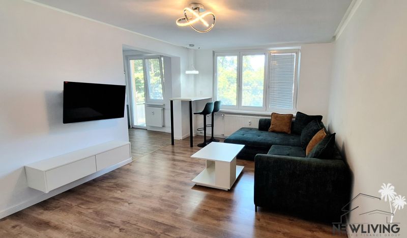 Living room of a two-room apartment with a wooden decor floor and a corner sofa.