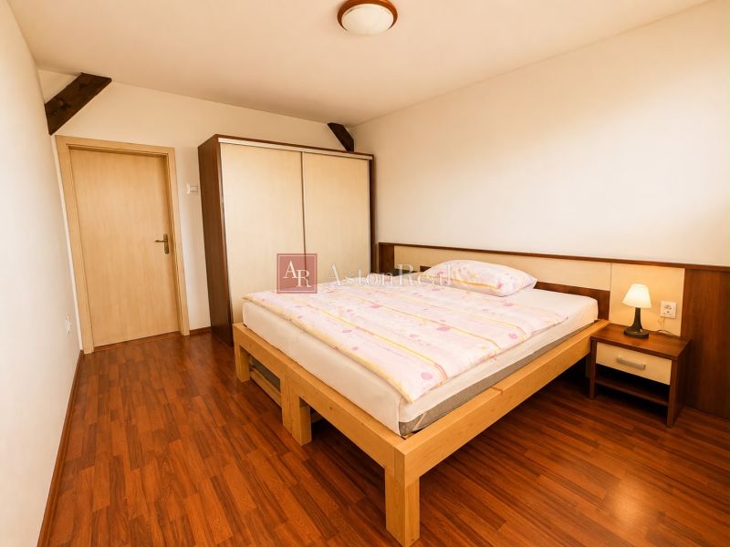 A bedroom in a three-room apartment with a wood-patterned floor, a large wardrobe, and a light-colored bed.