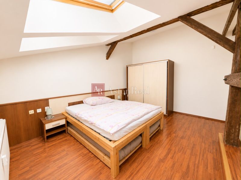 A bedroom in a three-room apartment with a wood-patterned floor, skylights, and wooden beams.