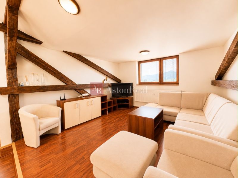 A bright living room with wood-patterned flooring, a corner sofa, and wooden beams.