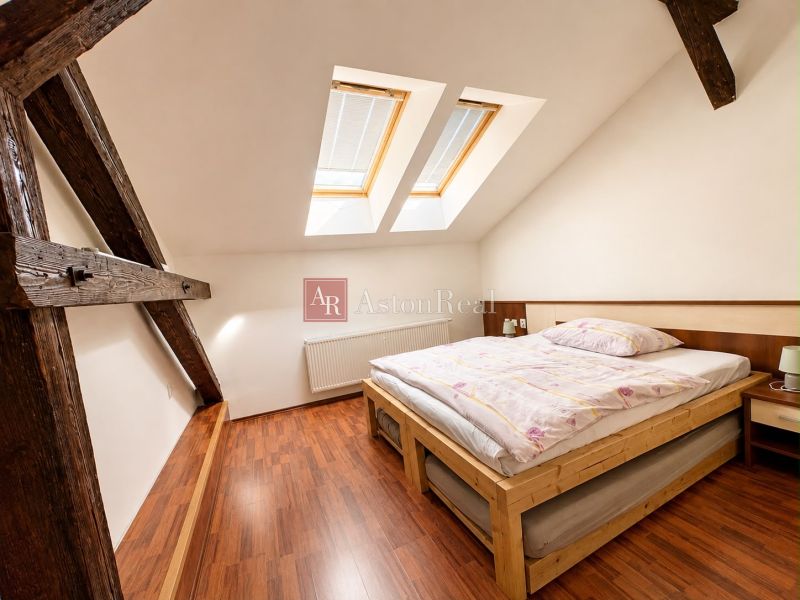 Attic bedroom with a bed, skylights, and a wooden decor floor in a 3-room apartment.