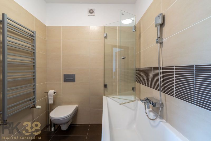 Bathroom in a holiday apartment with a bathtub, shower, and wall-hung toilet.