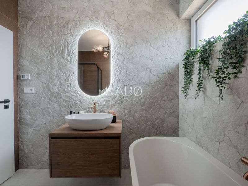 A bathroom in a family house with stone cladding, hanging plants, and a vessel sink.