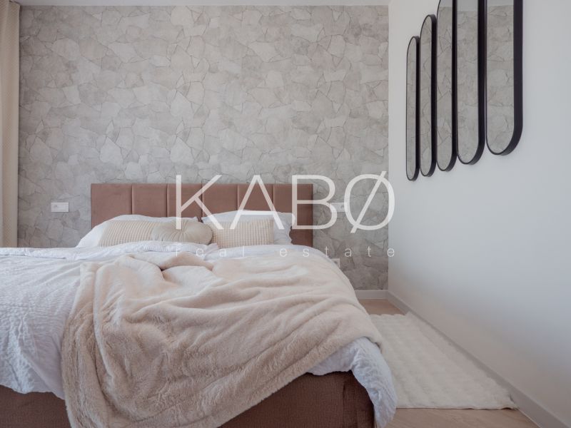 Bedroom in a family house with a patterned wall and mirrors, bed with a cream bedspread.