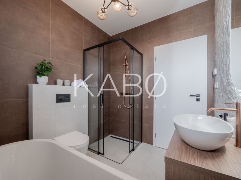 A family house bathroom with brown tiles, a shower corner, and a washbasin on a wooden decor.