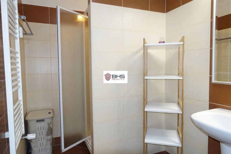 A bathroom in a two-room apartment with a shelf and a shower corner, tiles in brown tones.