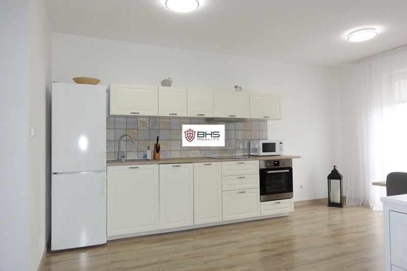 A kitchen in a 2-room apartment with a white kitchen unit and a floor with a wood decor.
