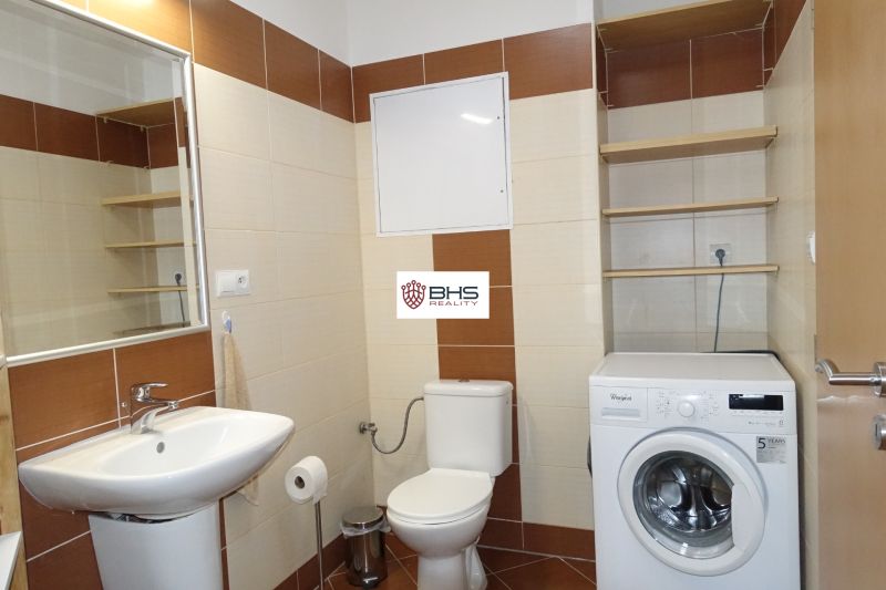 A bathroom in a 2-room apartment with a washing machine, sink, and shelves.