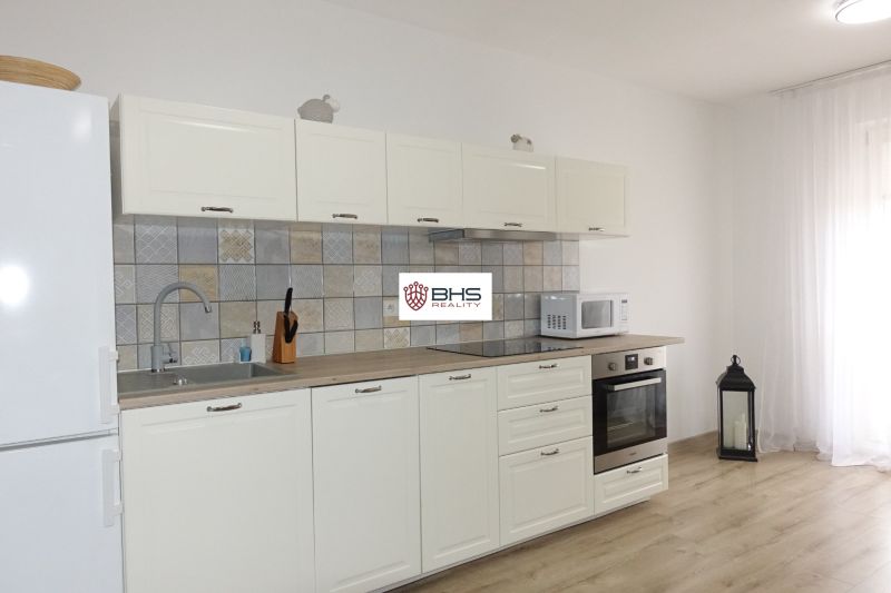 A kitchen unit in a 2-room apartment with a wooden decor floor, white furniture, and a built-in stove.