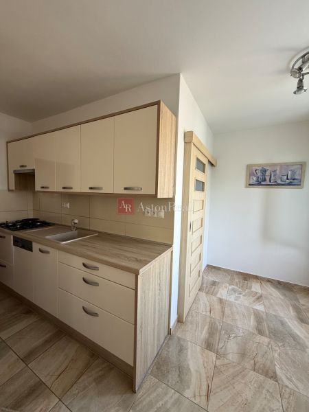 The kitchen of a 3-room apartment with a wooden decor floor and a light-colored kitchen unit.