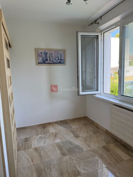 A room in a 3-room apartment with an open window, a light wall, and stone-design tiles.