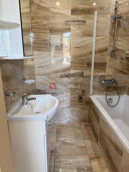 A bathroom with a bathtub and a sink, tiled with a brown marble decor in a 3-room apartment.