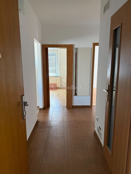 A hallway with a wooden decor floor leading to the rooms in a 3-room apartment.