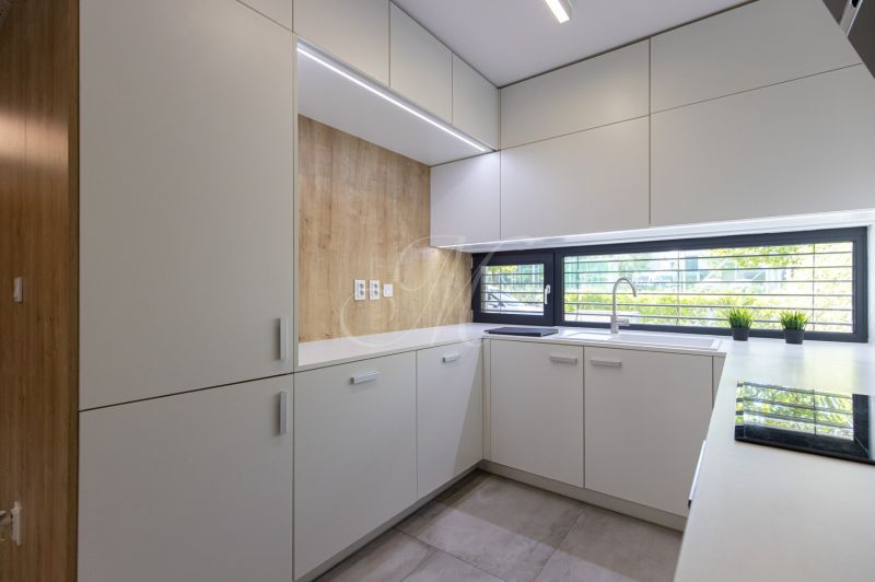 A kitchen in a 4-room apartment with a wooden decor floor, light furniture, and a large window.