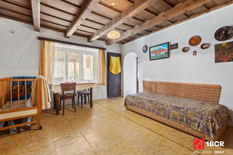 Interior of a family house with a wooden ceiling, bed, table, and chairs.