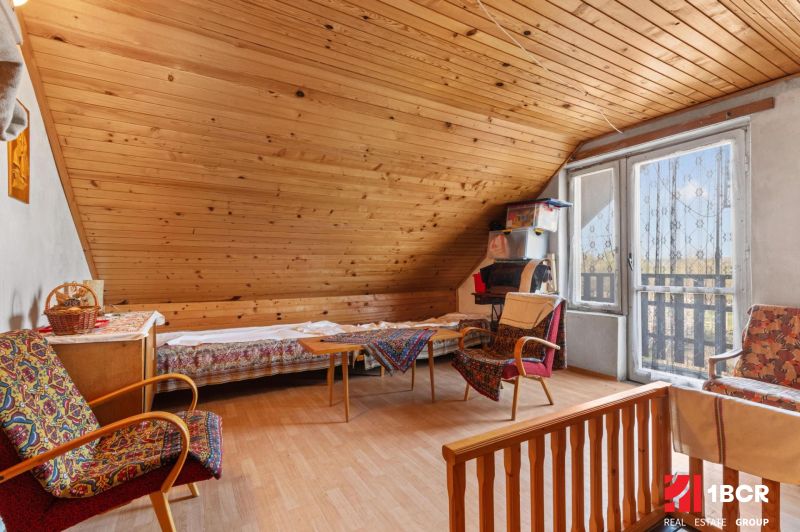 Attic room in a family house with a wooden decor floor, comfortable armchairs, and a dining table.