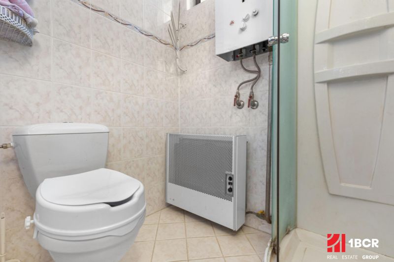 Toilet, shower corner, and gas heater in the bathroom of a family house.