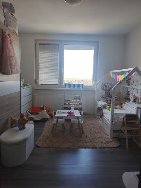 Children's room in a three-room apartment with a wooden decor floor, a play table, and a bed.