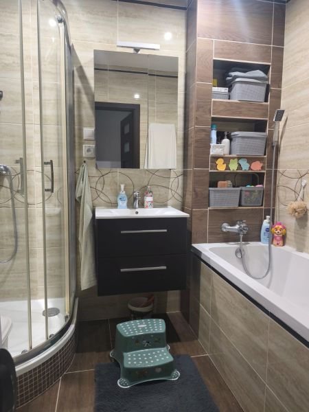 Bathroom with a bathtub, shower corner, and storage shelves in a 3-room apartment, floor with wood decor.