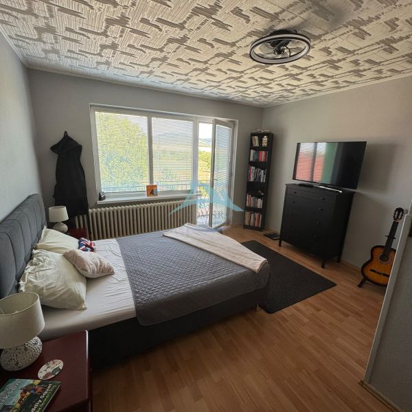 Bedroom in a family house with a wood-patterned floor, a bed, and a guitar.