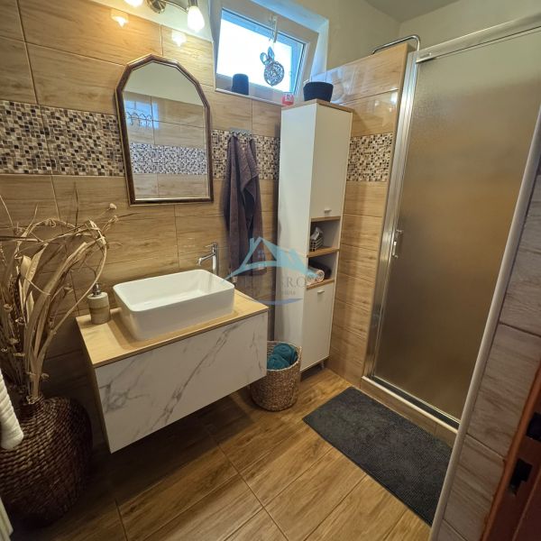 A bathroom in a family house with a sink, a shower, and a floor with a wooden decor.