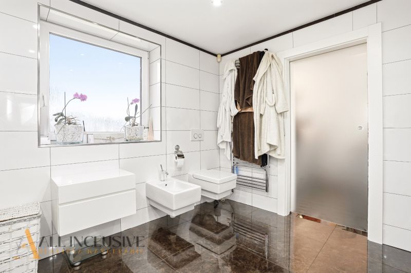 A bathroom in a family house with white tiles, modern fixtures, and plants on the windowsill.